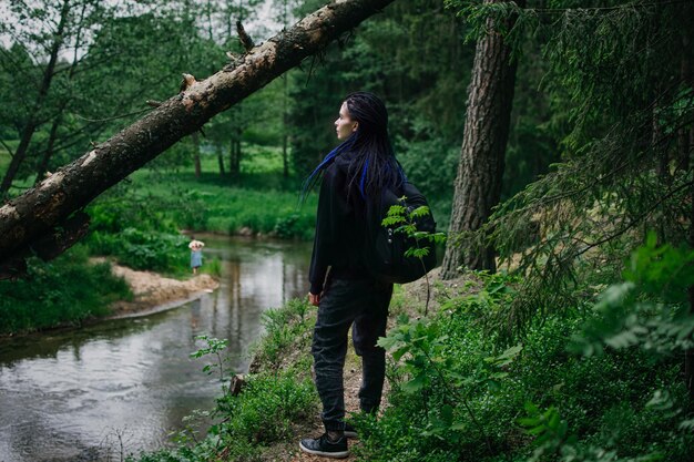 Chica viajera en el bosque mira el río Chica con rastas en el bosque Hippie