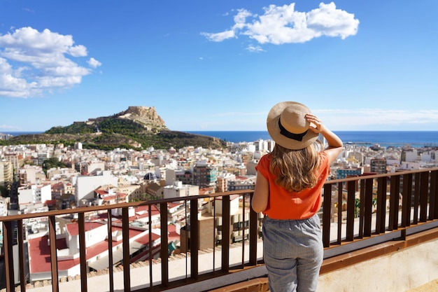 Chica viajera disfrutando de la vista del paisaje urbano de Alicante y el Monte Benacantil con el Castillo de Santa Bárbara y el mar al fondo, España