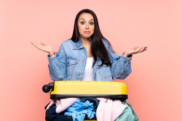 Chica viajera con una maleta llena de ropa de color rosa que tiene dudas con expresión de la cara confusa