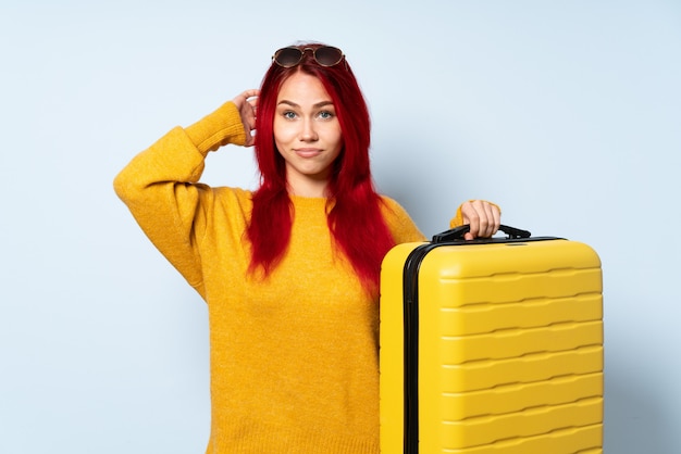 Chica viajero sosteniendo una maleta aislada en azul con dudas