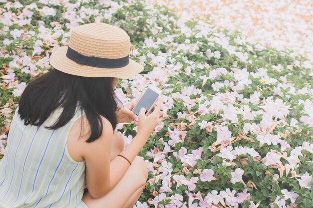 Chica de viajero usando teléfono inteligente en el fondo del jardín de flores con filtro vintage