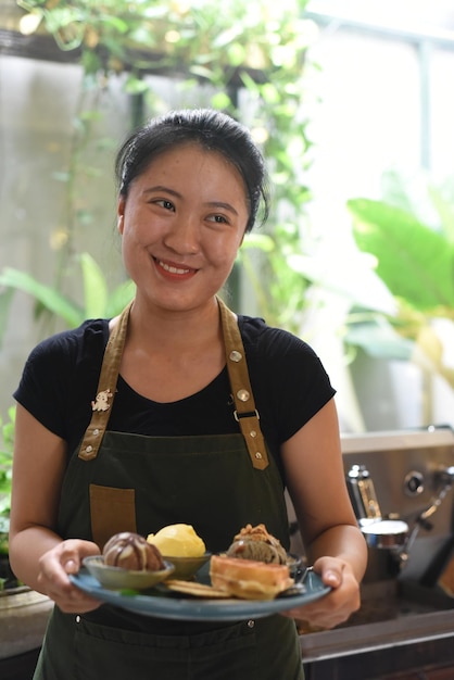 Chica vietnamita sirviendo helado casero con gofres en una cafetería.