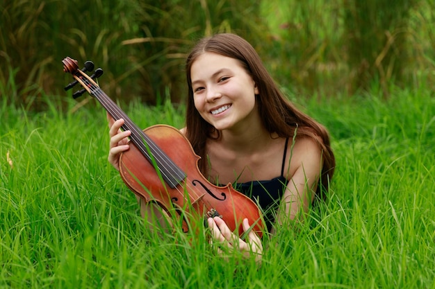 Una chica con un violín yace en la hierba.