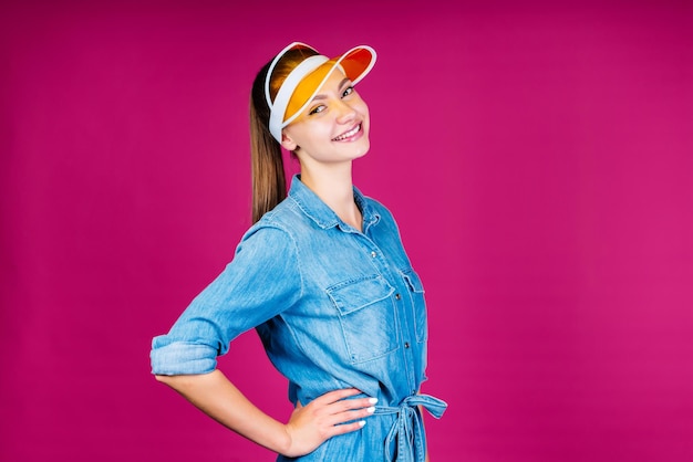 La chica de la visera sonríe con benevolencia con la cabeza hacia atrás y el fondo akimbo rosa