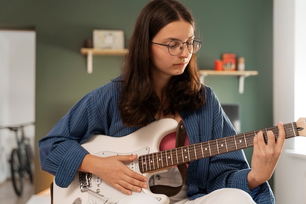 Foto chica de vista frontal tocando la guitarra en casa