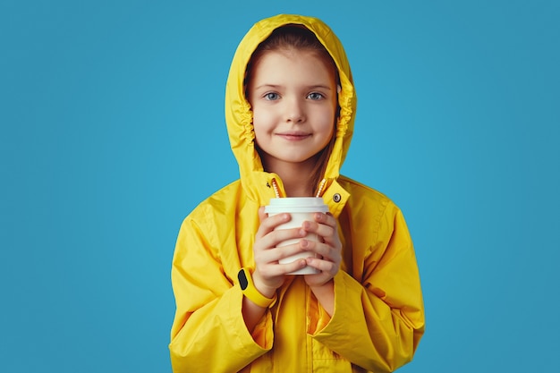 Chica viste impermeable amarillo sostiene la taza con té intenta calentar mientras bebe