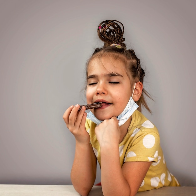 Chica vistiendo su mascarilla de medicina y comiendo barras de chocolate con placer