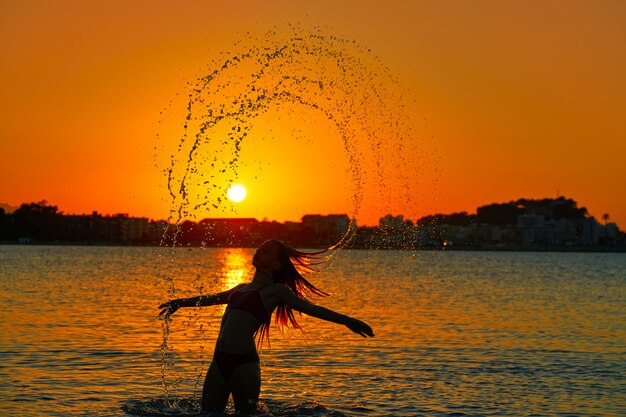 Chica volteando el pelo tirón en la playa de la puesta del sol