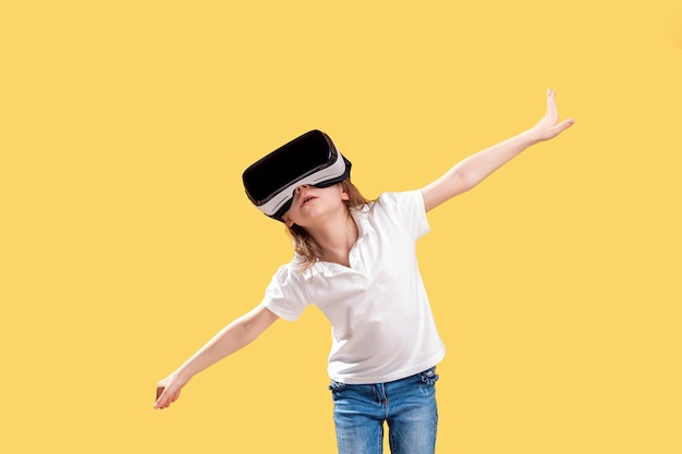 Chica yo en traje formal con gafas VR poniendo manos en emoción aislado en amarillo. Niño usando un dispositivo de juego para realidad virtual. Tecnología virtual