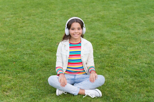 Chica de yoga niño pequeño en auriculares lista de reproducción de verano disfrutar de la naturaleza de primavera al aire libre niño estudiar audio libro nueva tecnología Niño escuchar música en hierba verde Estilo de vida saludable y relajarse