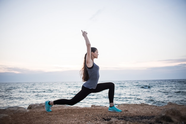 Chica yogui en pose de guerrero en un acantilado junto al mar