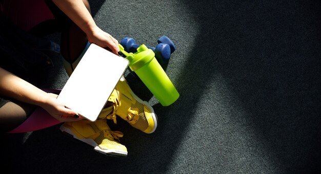 chica con zapatillas amarillas sostiene una tableta con pesas y una botella de agua para entrenar. Concepto de aprendizaje en línea.