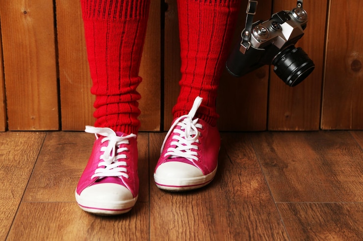 Foto chica en zapatillas de deporte con cámara de fotos retro en la habitación