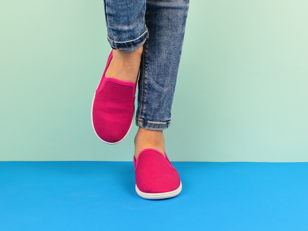 Foto chica en zapatillas rojas y pantalones rotos caminando sobre el piso azul.