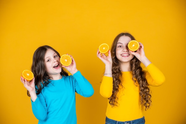Chicas adolescentes sonrientes sostienen fruta naranja sobre fondo amarillo