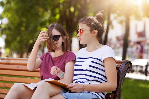 Chicas alegres y felices están en el parque para disfrutar del ambiente veraniego y leer las últimas noticias del mundo.