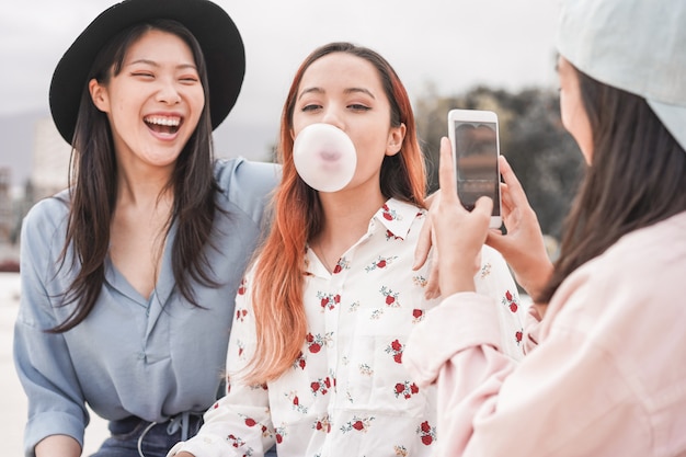 Chicas asiáticas felices haciendo video historia para la aplicación de red social al aire libre - Amigas jóvenes divirtiéndose haciendo transmisiones en vivo - Nuevas tendencias tecnológicas y concepto de amistad - Centrarse en la persona que sopla