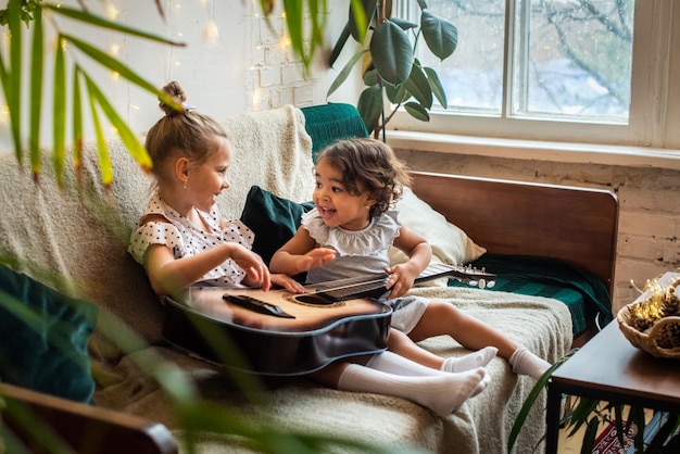 Chicas blancas y negras en un sofá cama y tocan la guitarra, las chicas tocan, componen melodía y música.