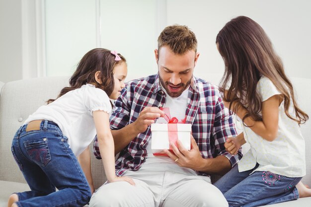 Chicas curiosas mirando al padre abriendo un regalo