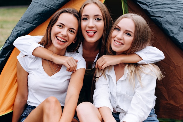 Chicas divertidas abrazándose y sonriendo felizmente sentados en el campamento