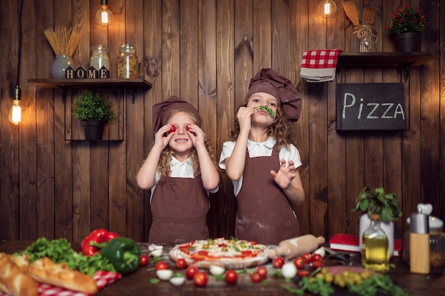 Chicas divertidas cocinando pizza y engañando con tomate y lechuga