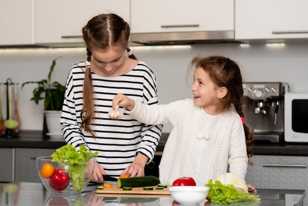 Las chicas de dos lindas hermanas cortan una ensalada de verduras frescas. Comida sana. Infancia.