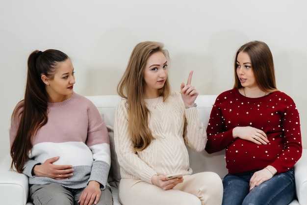 Las chicas embarazadas se sientan en el sofá y se divierten charlando entre ellas. Embarazo y cuidado del futuro del niño.