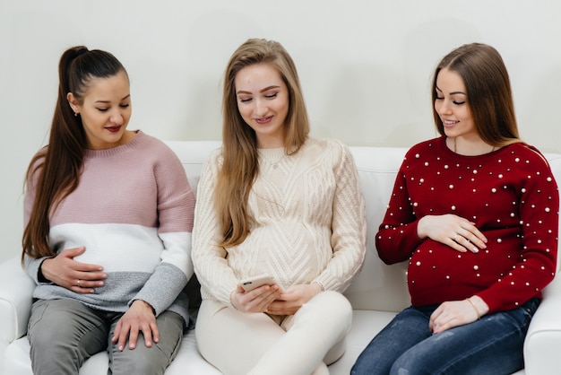 Las chicas embarazadas se sientan en el sofá y se divierten charlando entre ellas. Embarazo y cuidado del futuro del niño.