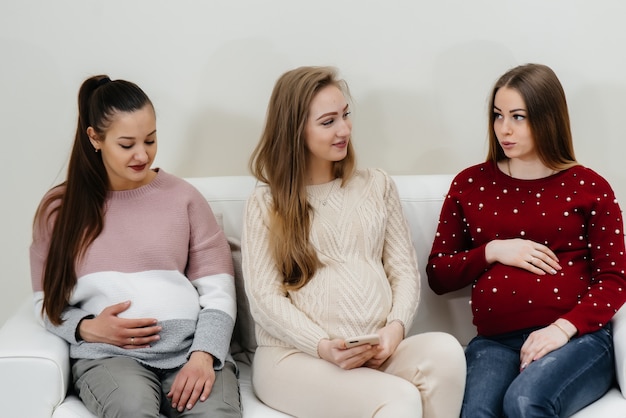 Las chicas embarazadas se sientan en el sofá y se divierten charlando entre ellas. Embarazo y cuidado del futuro del niño.