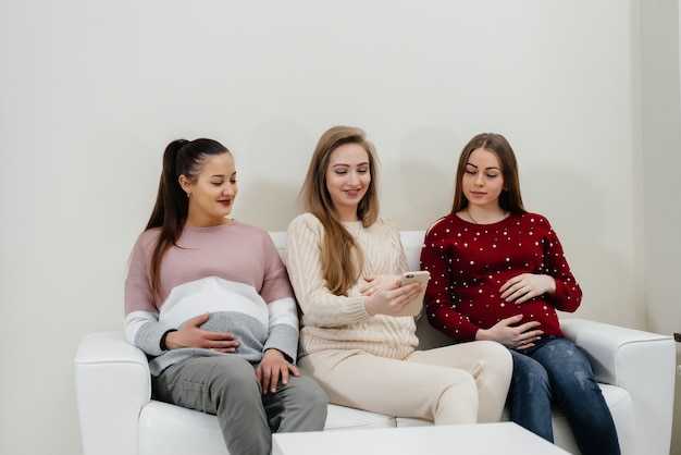 Las chicas embarazadas se sientan en el sofá y se divierten charlando entre ellas. Embarazo y cuidado del futuro del niño.