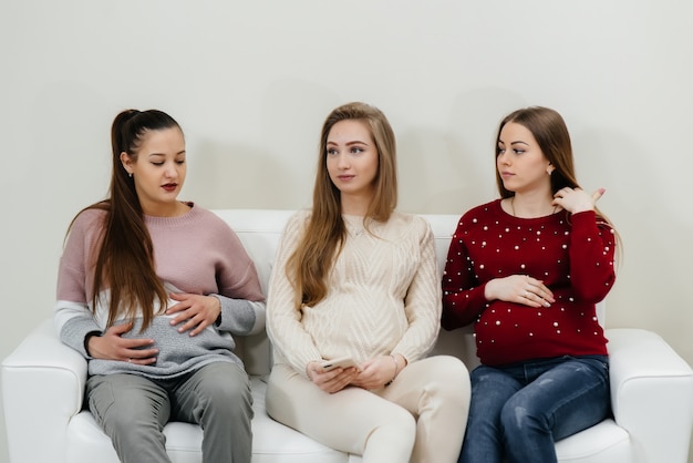 Las chicas embarazadas se sientan en el sofá y se divierten charlando entre ellas. Embarazo y cuidado del futuro del niño.