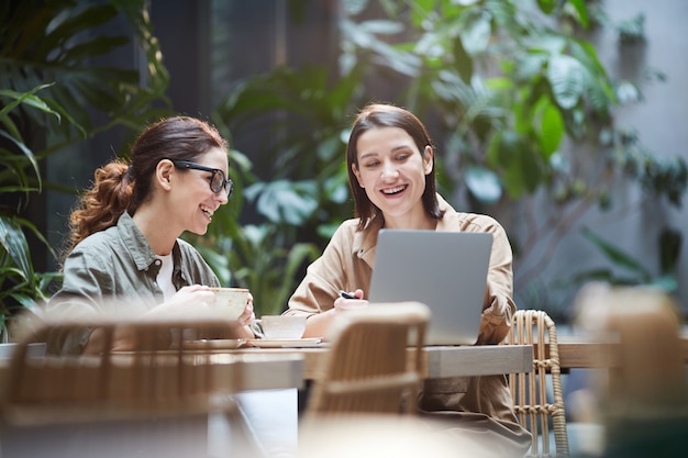 Chicas emocionadas analizando datos en línea en café