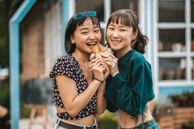 Chicas emocionadas comiendo juntas un sándwich y luciendo entretenidas