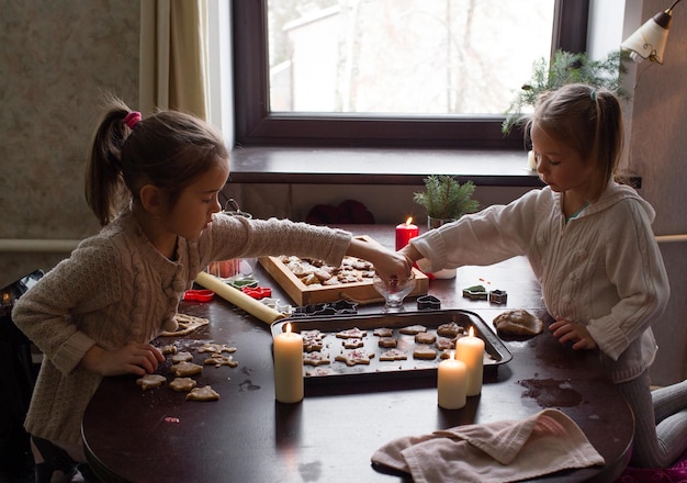 Chicas encantadoras cocinan galletas navideñas juntas en casa en la mesa