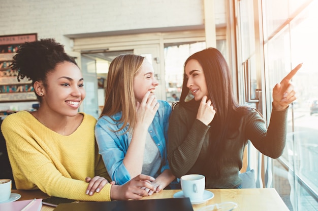 Estas chicas están chismorreando. Simplemente sentadas en la mesa del café y hablando de otra chica. Las mujeres jóvenes están asombradas y tratan de decirse unas a otras sobre lo que piensa sobre la situación.