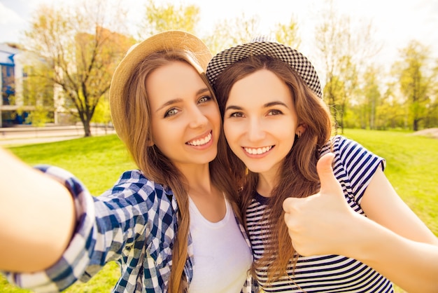 Chicas guapas con sonrisas radiantes disparando y mostrando el pulgar hacia arriba