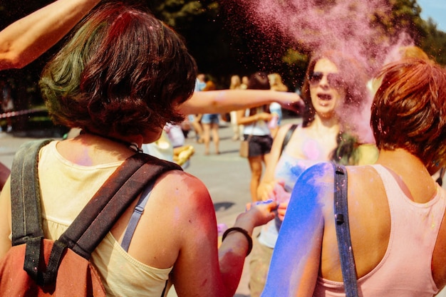 Chicas hipster felices divirtiéndose con polvo colorido en el festival de colores holi fest en verano