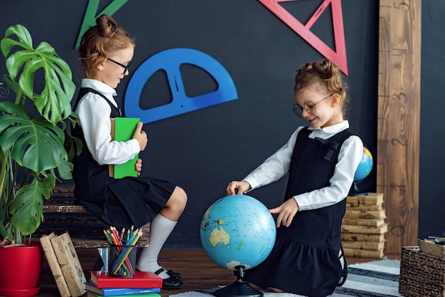 Chicas inteligentes que leen libros y examinan el globo en la escuela