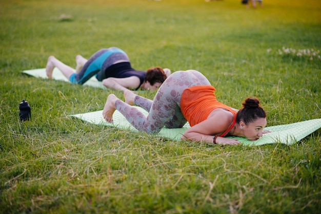 Las chicas jóvenes hacen yoga al aire libre en el parque durante el atardecer. Estilo de vida saludable