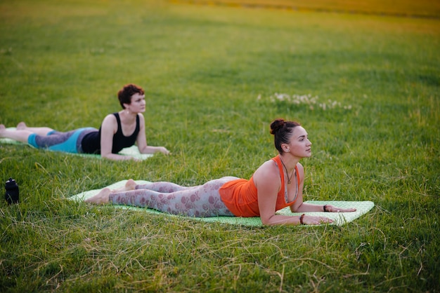 Las chicas jóvenes hacen yoga al aire libre en el parque durante el atardecer. Estilo de vida saludable