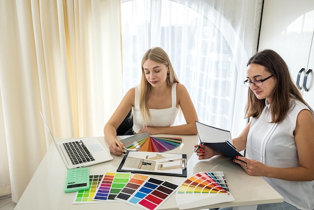 Las chicas jóvenes en la mesa se sientan y eligen entre las muestras de color necesarias para el diseño del hogar