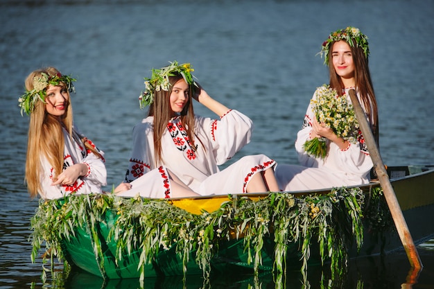 Las chicas jóvenes con trajes nacionales navegan en un bote decorado con hojas y crecimientos. Fiesta eslava de Ivan Kupala.