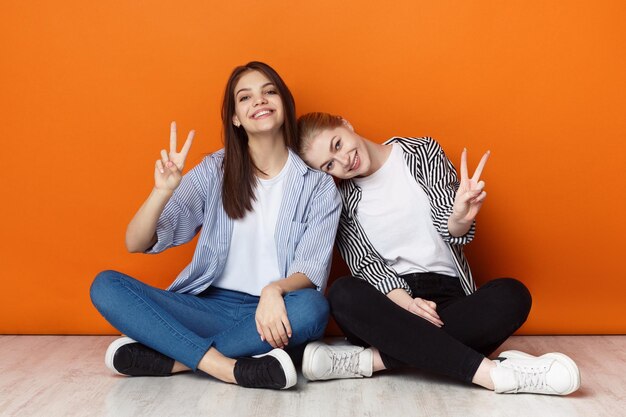 Chicas juguetonas mostrando gestos de paz sentadas en el suelo