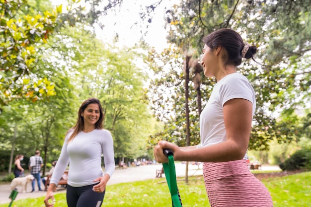 Foto chicas latinas haciendo deporte en un parque verde atento constructor con los estudiantes en el ejercicio de las correas elásticas