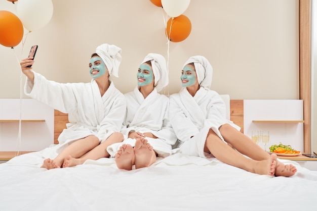 Foto chicas con máscaras cosméticas tomando selfie en dormitorio.