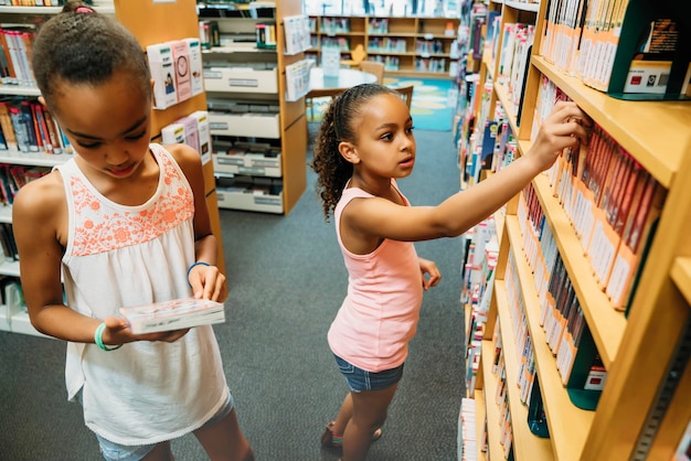 Chicas mirando libros en la biblioteca pública