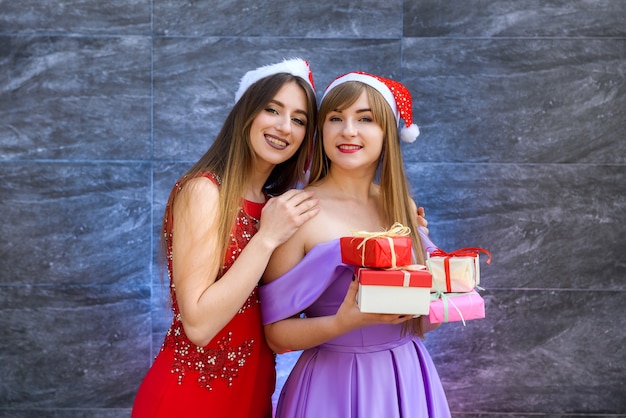 Chicas de moda en elegantes vestidos de noche posando con cajas de regalo. Concepto de celebración de año nuevo