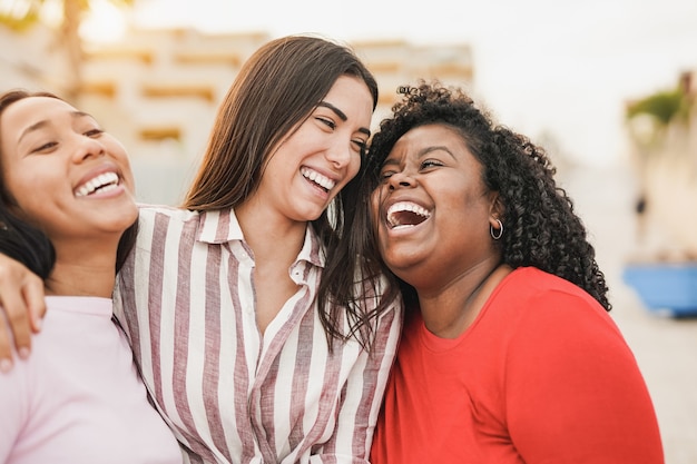 Chicas multirraciales riendo juntas en la ciudad mientras se abrazan - Jóvenes mujeres latinas al aire libre