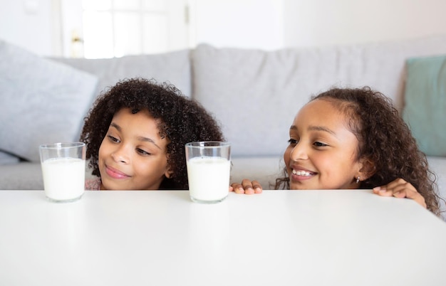 Chicas negras mirando vasos de leche en la mesa en casa