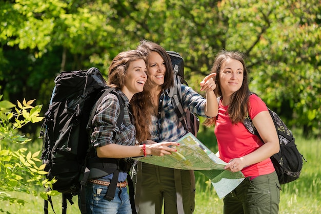 Chicas turísticas en el bosque con mapa y mochilas.